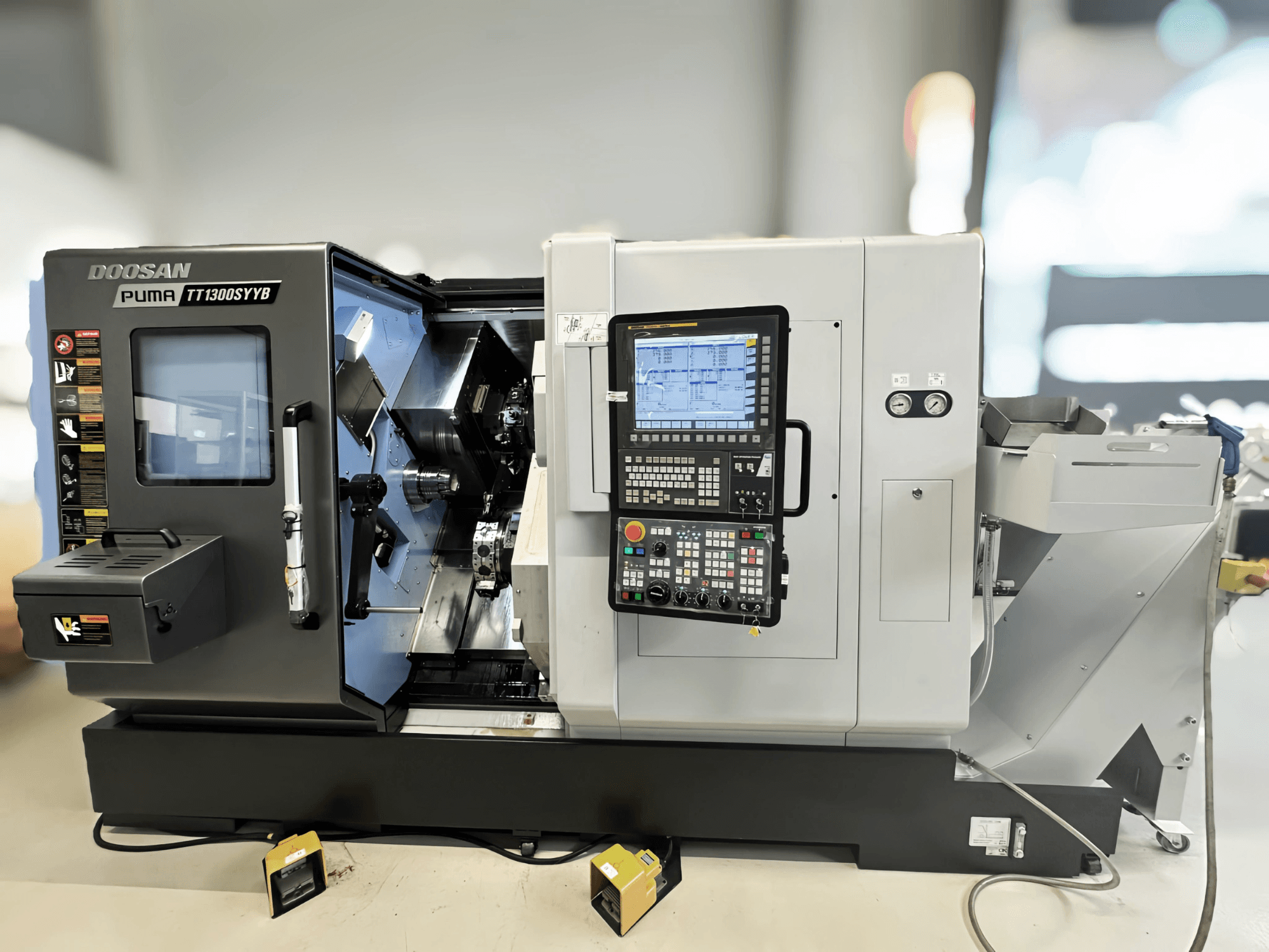 Centro de torneado y fresado Doosan Puma TT1300SYYB en vista lateral, mostrando el panel de control y el interior de la máquina con las herramientas visibles.