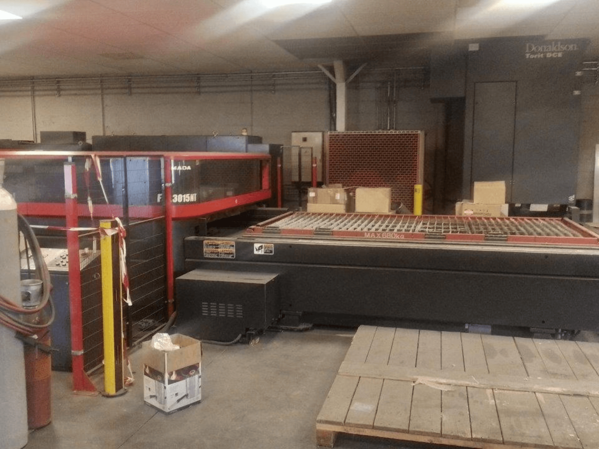 Máquina de corte por láser de CO₂ AMADA FOL 3015 NT, vista frontal; cabina de seguridad roja, mesa de trabajo con rejilla, entorno industrial.