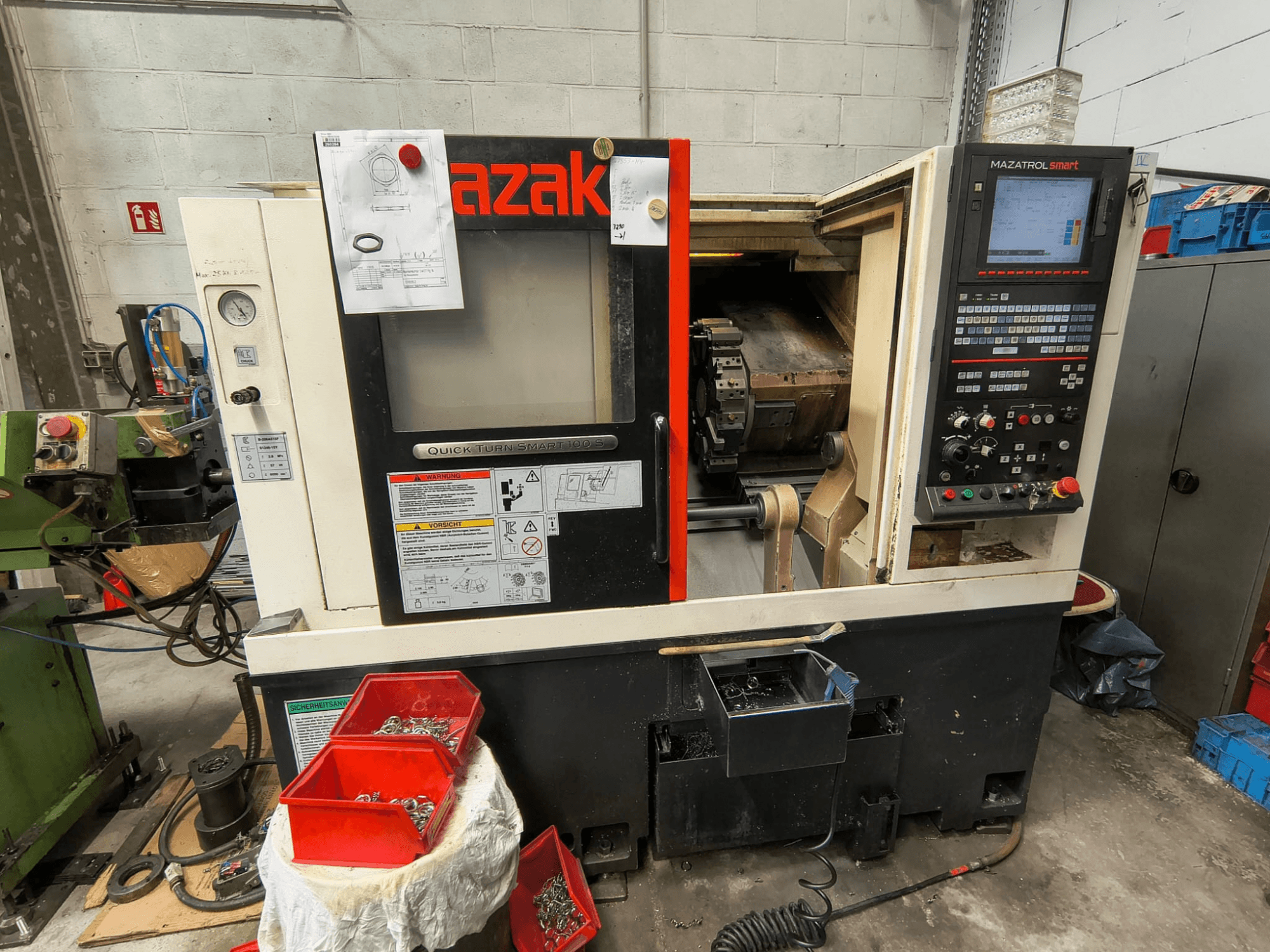 Mazak Quick Turn Smart 100 S, vista lateral en la que se aprecian el panel de control, la bandeja de refrigerante y los compartimentos de almacenamiento con tornillos.