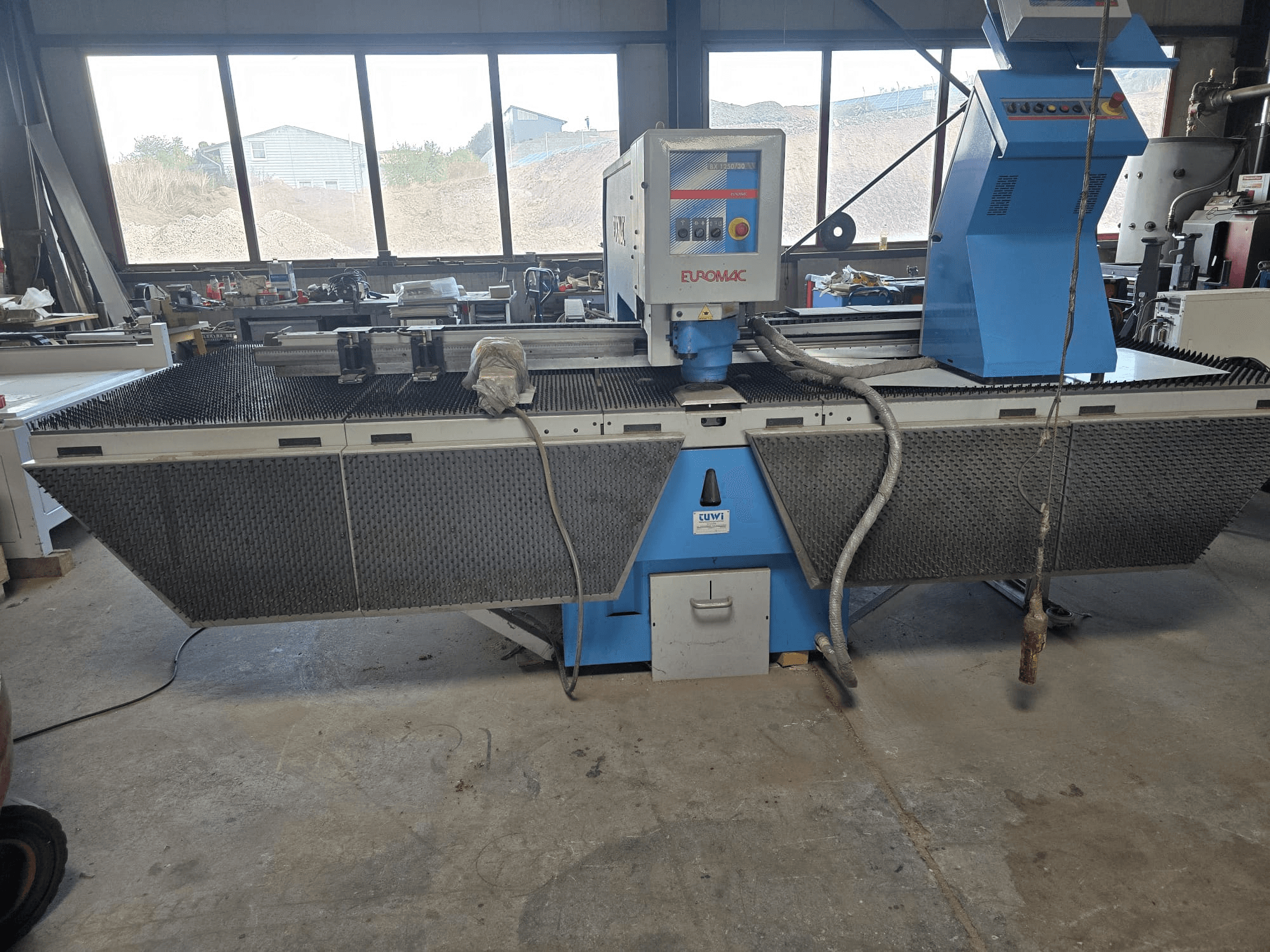 Máquina punzonadora CNC Euromac BX 1250/30 en un taller; vista lateral en la que se aprecian los mandos de la máquina, su diseño industrial y la bancada de corte de metal.