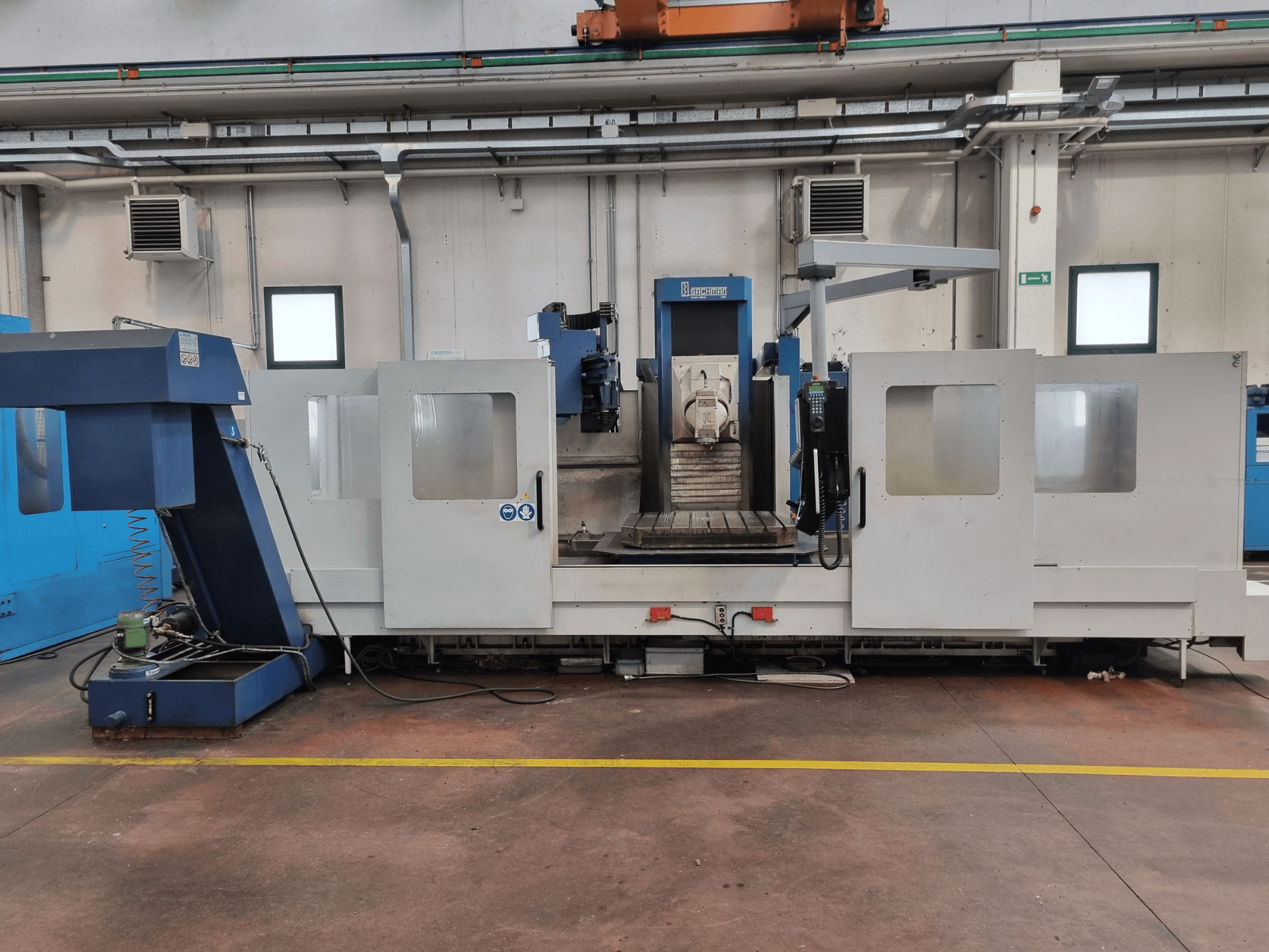 Fresadora CNC de "Brembana", vista lateral que muestra el panel de control y la zona operativa con una mesa de trabajo en el interior.