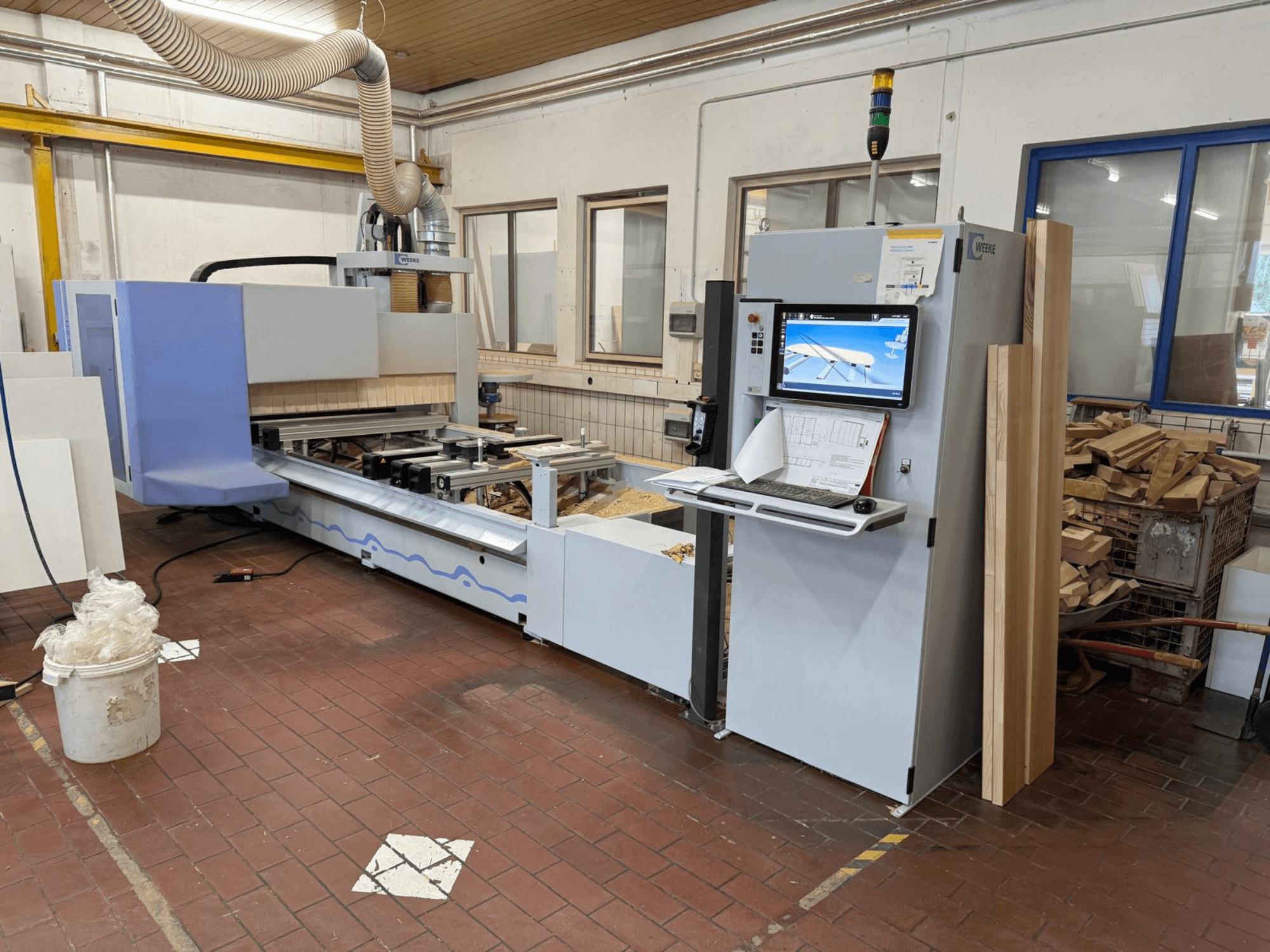 Centro de mecanizado CNC para madera Weeke PROFI BMG211/32/12/K, vista frontal, con panel de control y piezas de madera, y sistema de extracción de polvo.