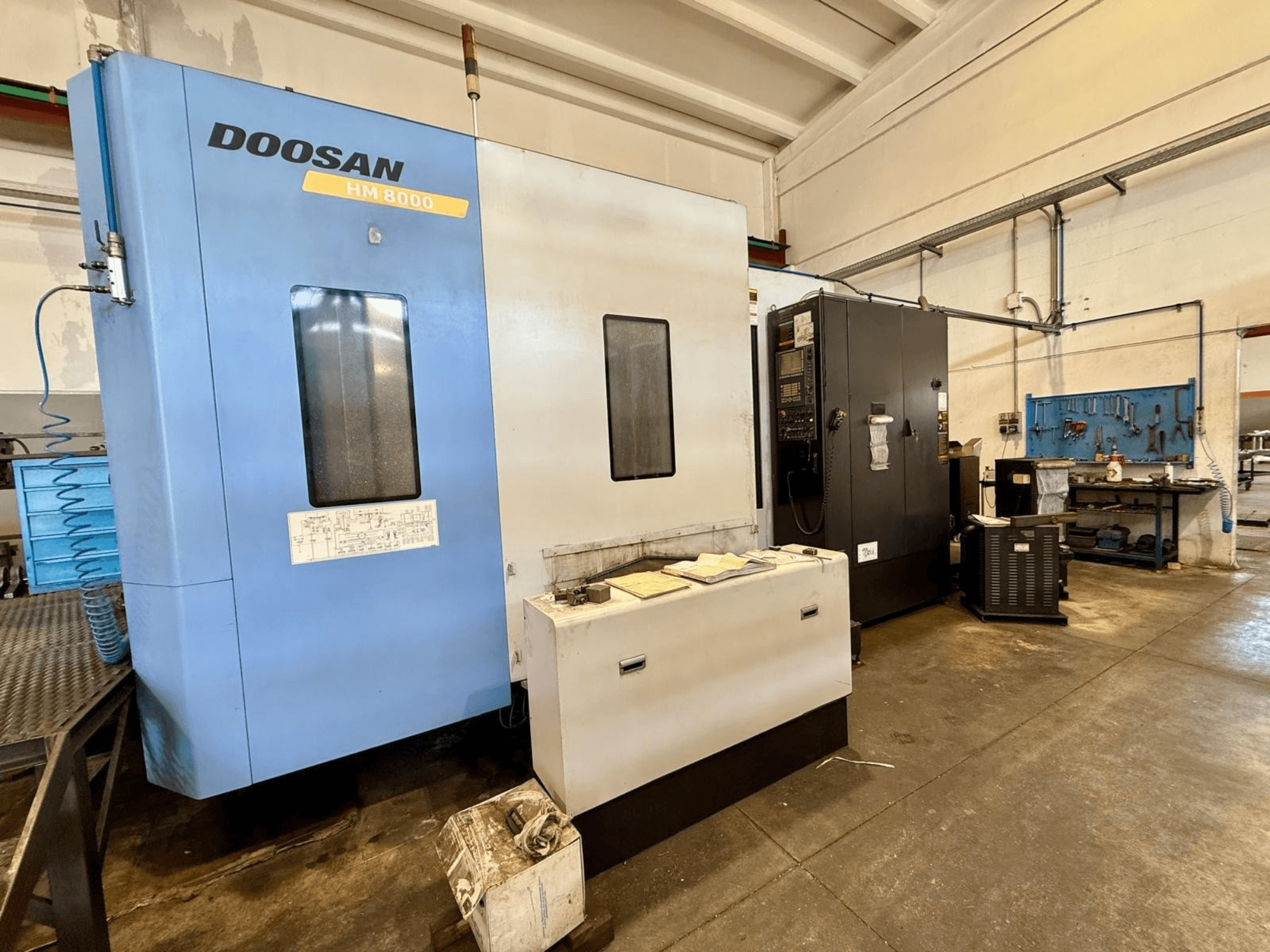 Centro de mecanizado horizontal DOOSAN HM 8000 de color azul, vista frontal, en la que se aprecian el panel de control y el equipamiento del taller que lo rodea.