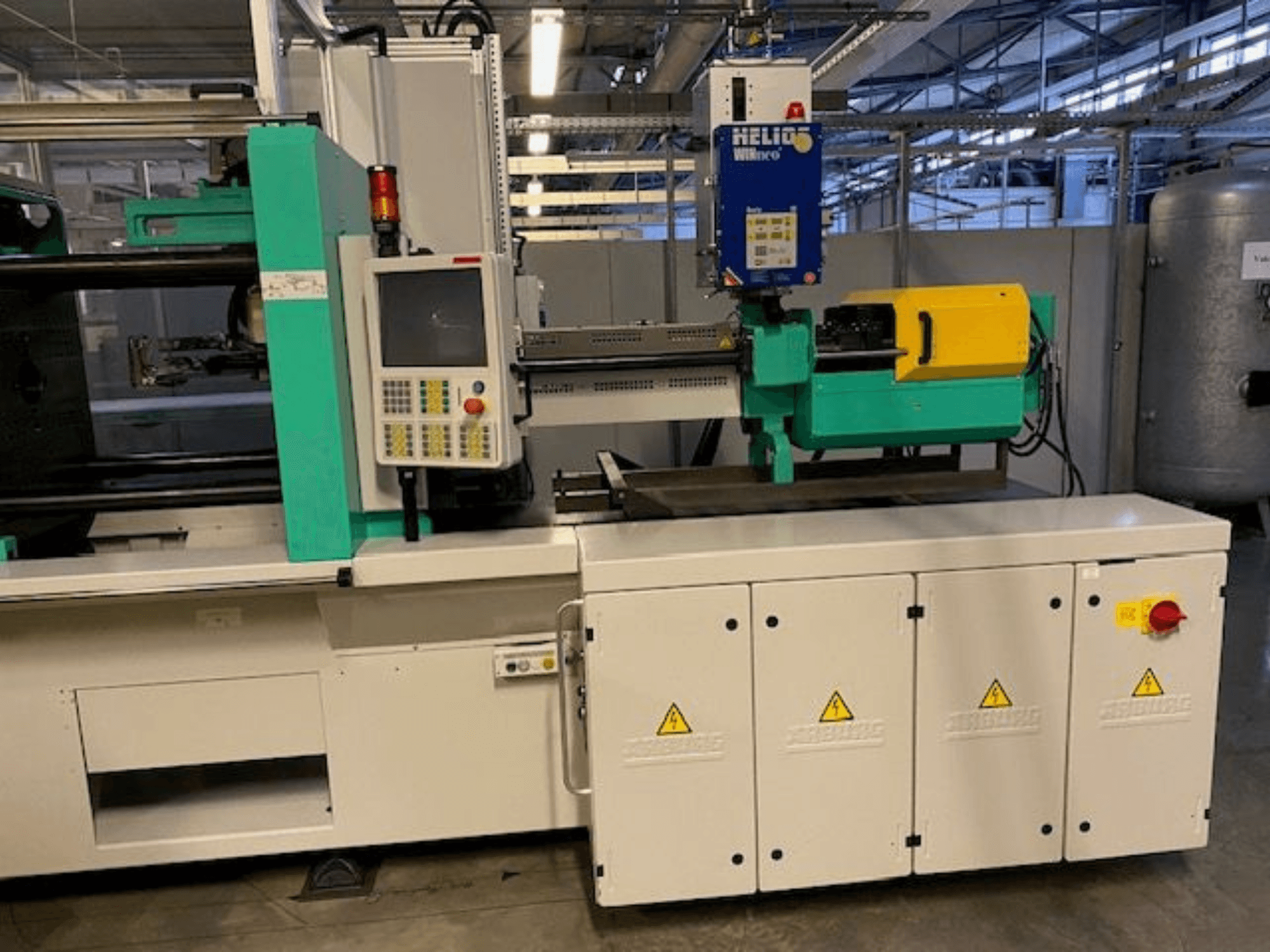 Máquina industrial de moldeo por inyección, modelo HELIO, vista frontal, con panel de control, protecciones de seguridad y botón de parada de emergencia.