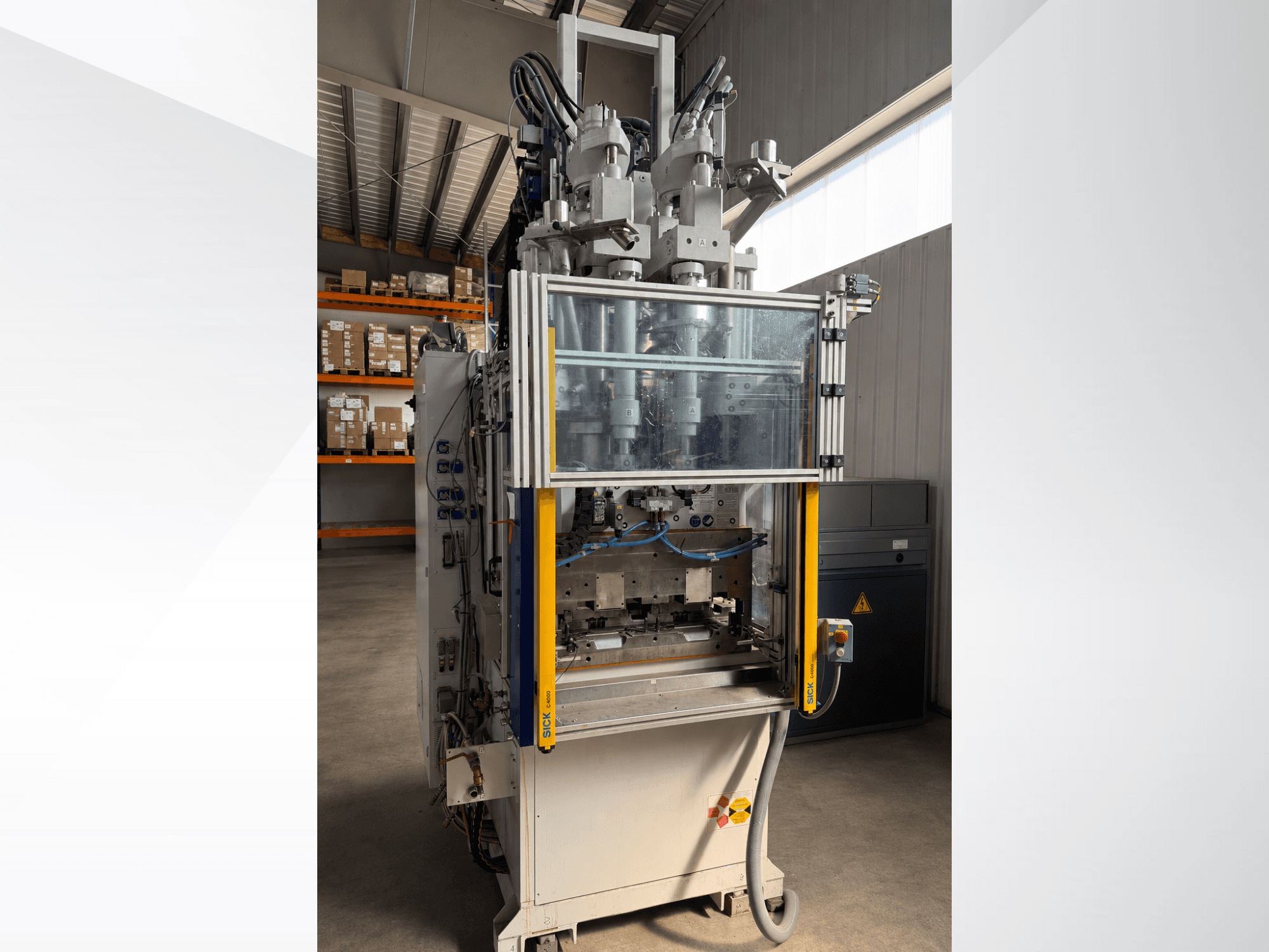 Máquina de moldeo por inyección vertical Battenfeld CM 40, vista frontal con panel transparente, en la que se aprecian el panel de control y los componentes de inyección.
