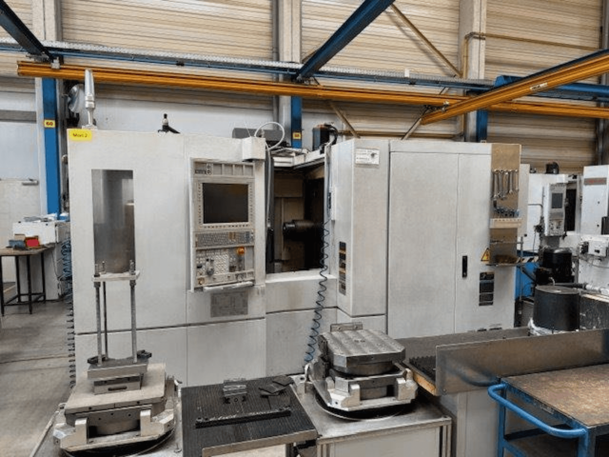 Vista frontal MORI SEIKI NH4000 DCG de un centro de mecanizado horizontal con panel de control y piezas sobre la mesa.