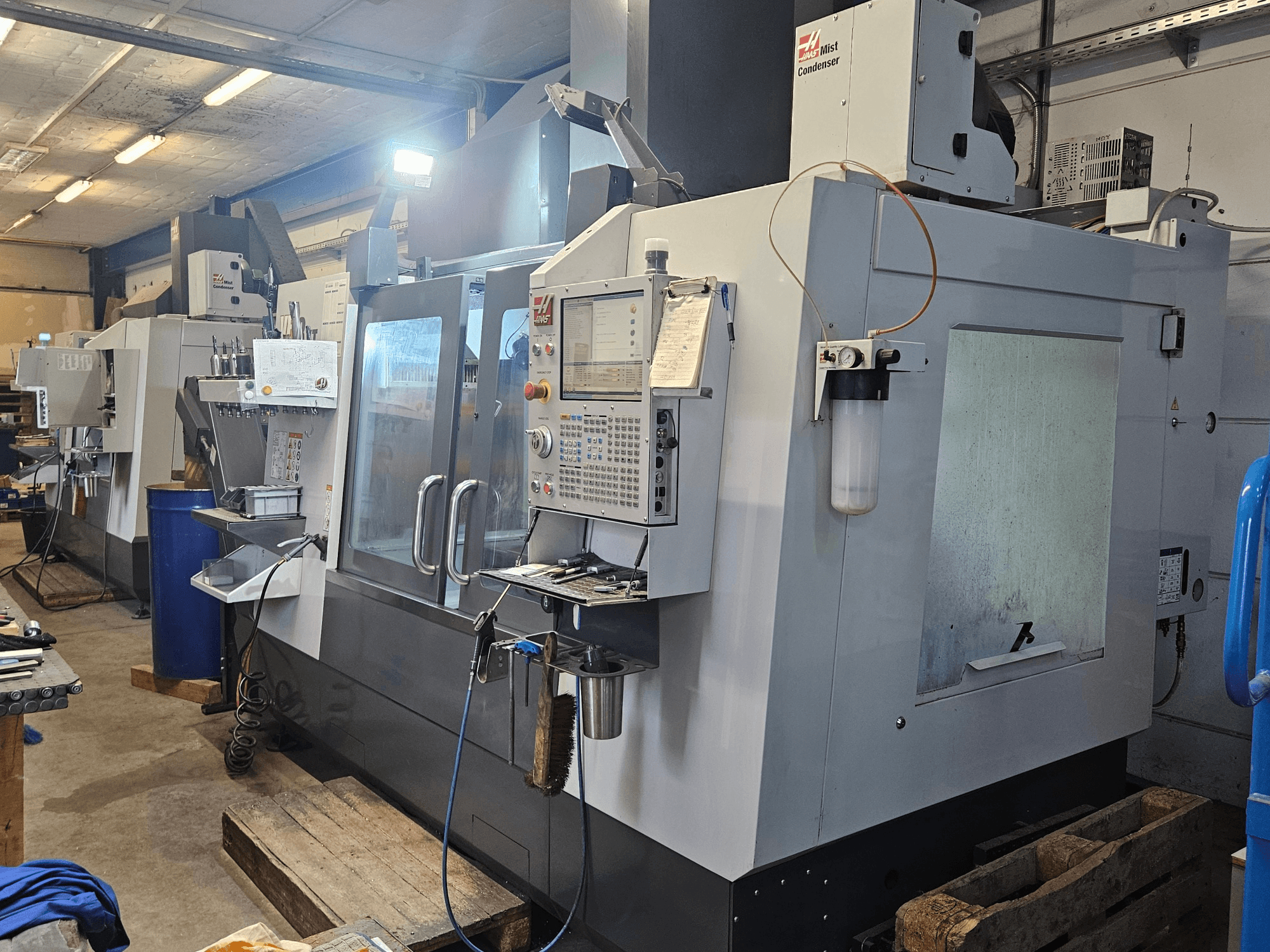 Centro de mecanizado vertical Haas VF-3YT/50 en un taller; vista frontal en la que se aprecian el panel de control, los portaherramientas y el condensador de neblina.