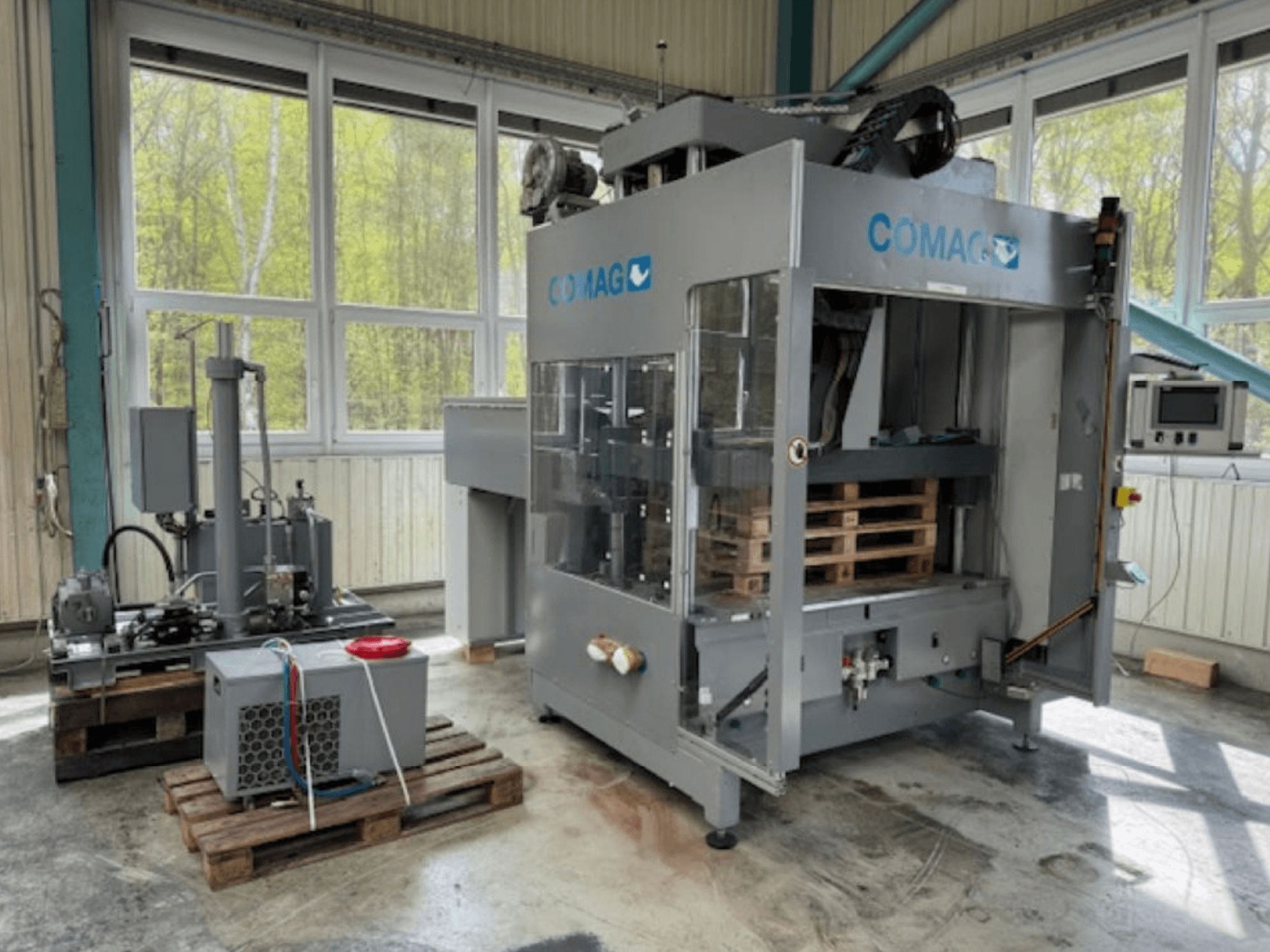Envolvedora de palets COMAG en un entorno industrial, vista frontal; se aprecian los palets y los componentes hidráulicos.