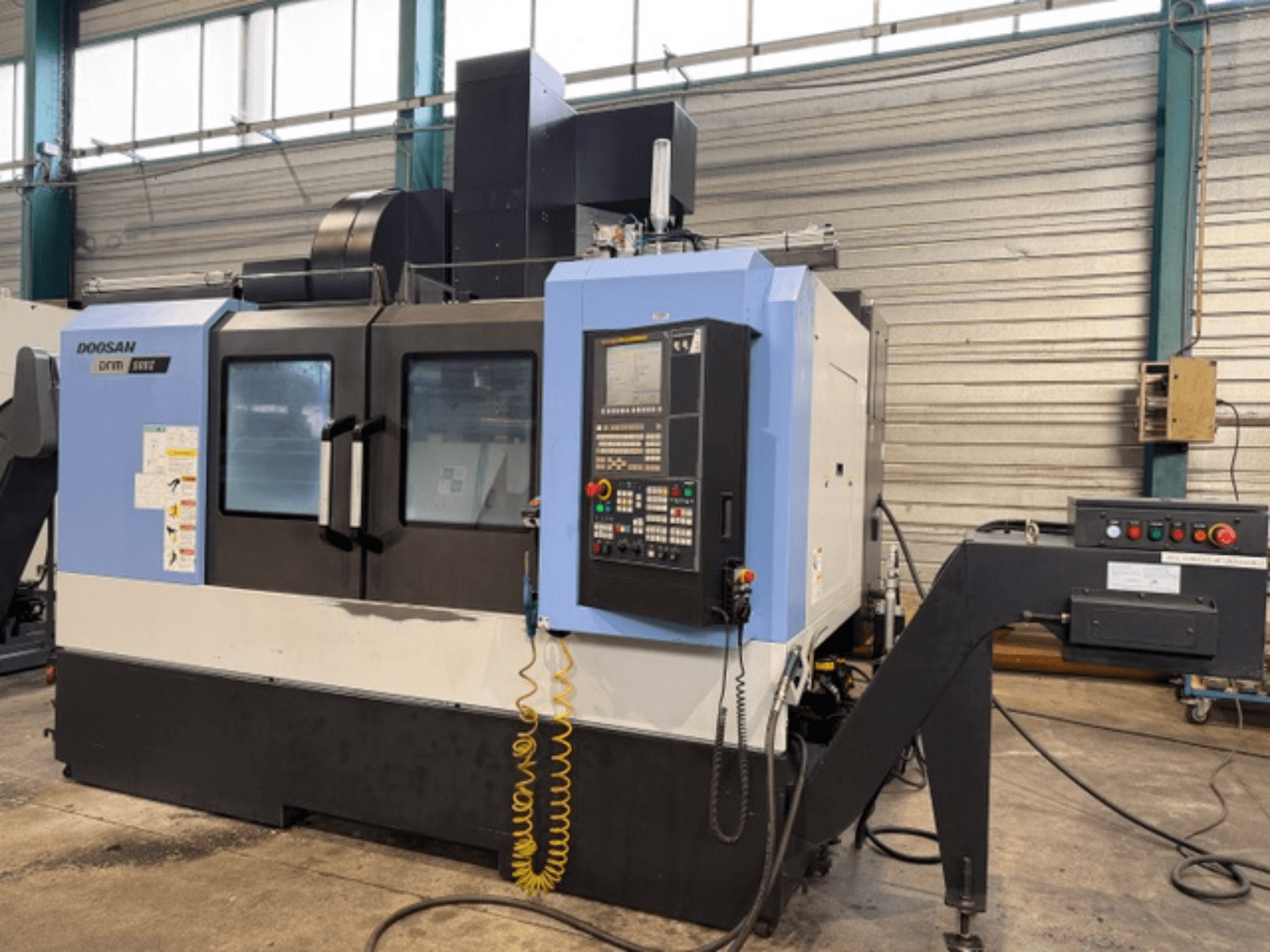 Fresadora CNC Doosan DNM 500II en vista frontal, con panel de control y portaherramientas, en un entorno de fábrica.