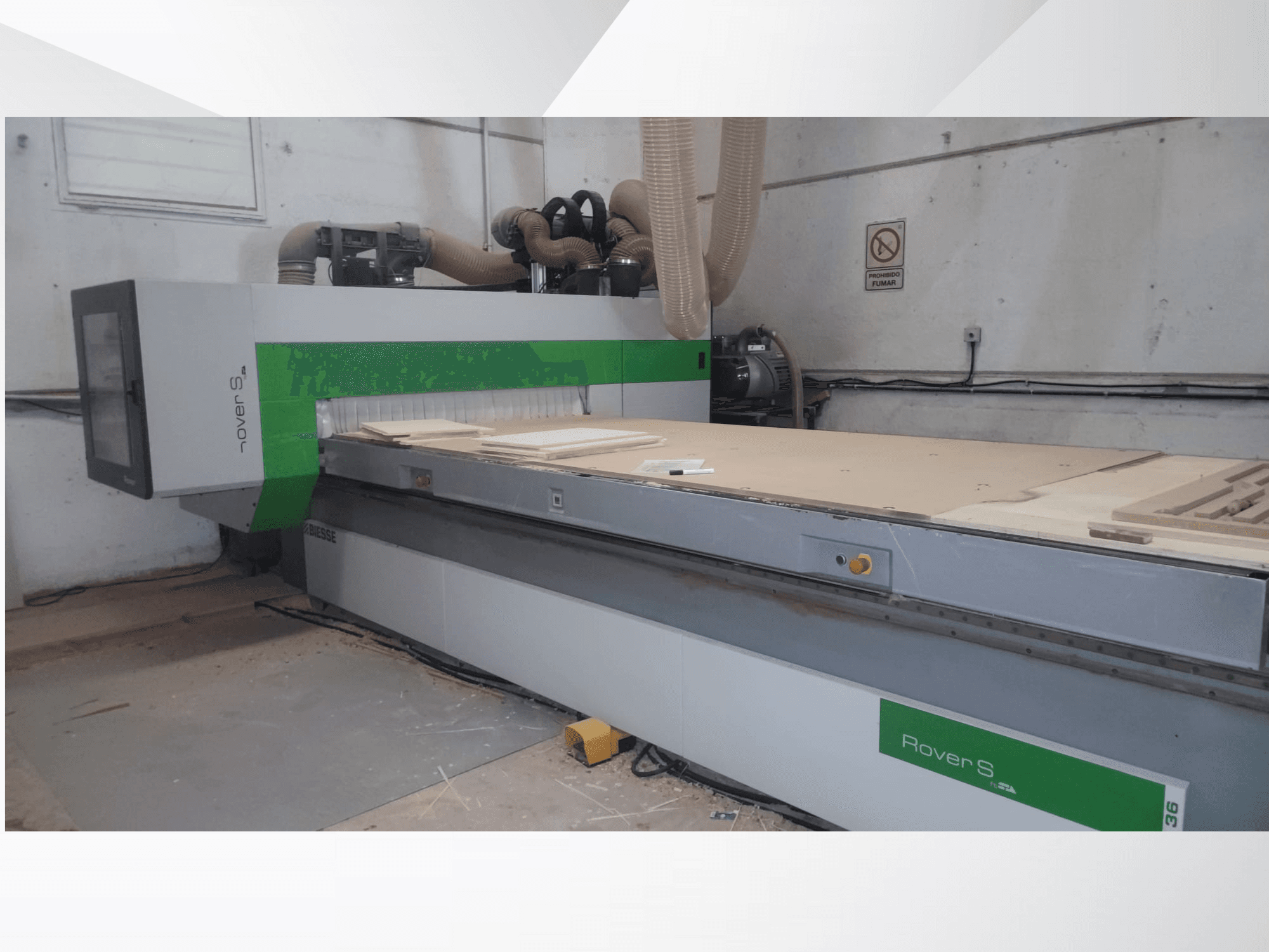 Vista frontal de la máquina CNC Rover S de Biesse, con una gran superficie de trabajo con paneles de madera y mangueras de extracción de polvo.