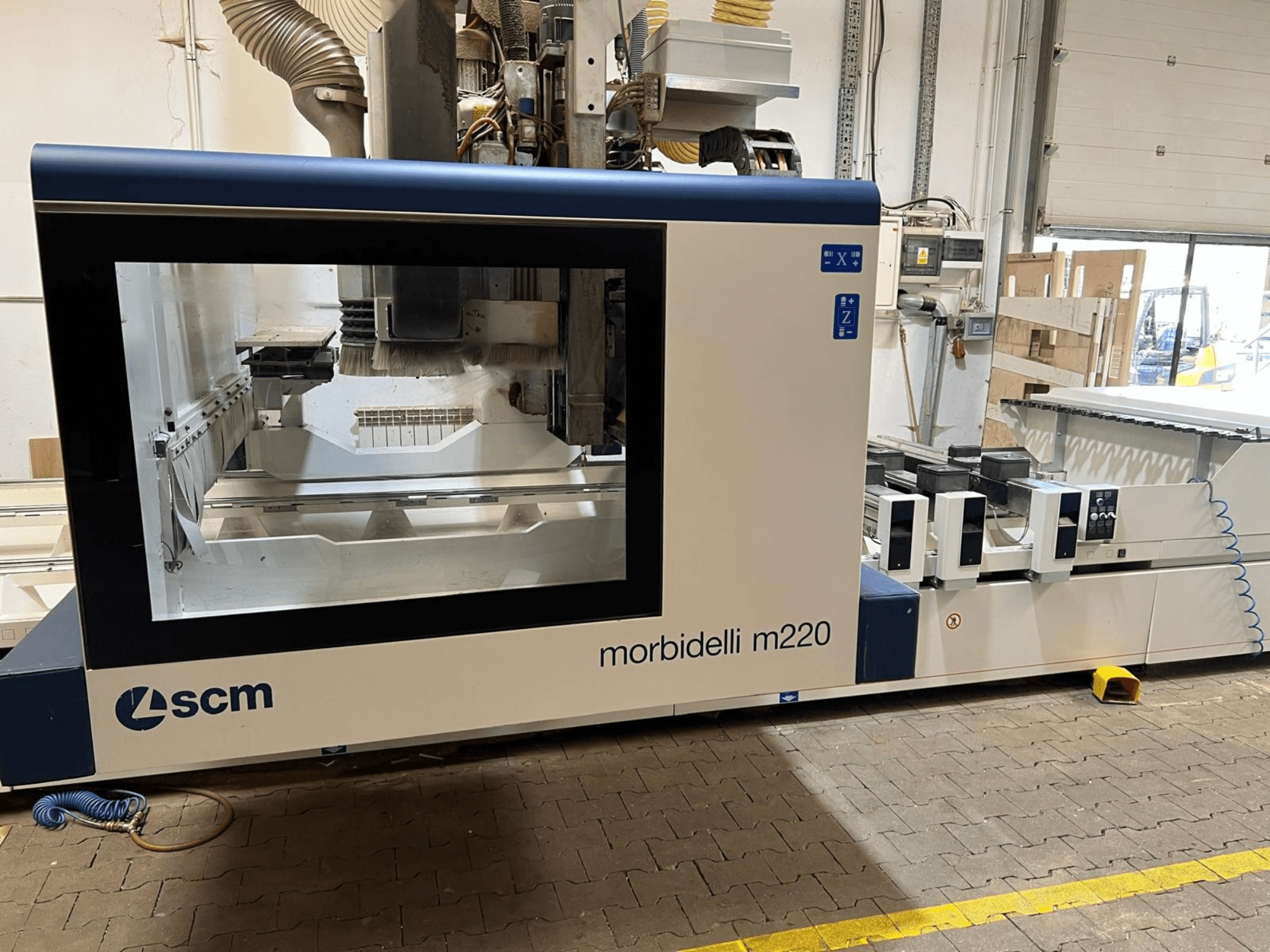 Vista frontal del centro de mecanizado CNC SCM Morbidelli M220, en la que se aprecian una amplia ventana, el panel de control y la zona de trabajo.