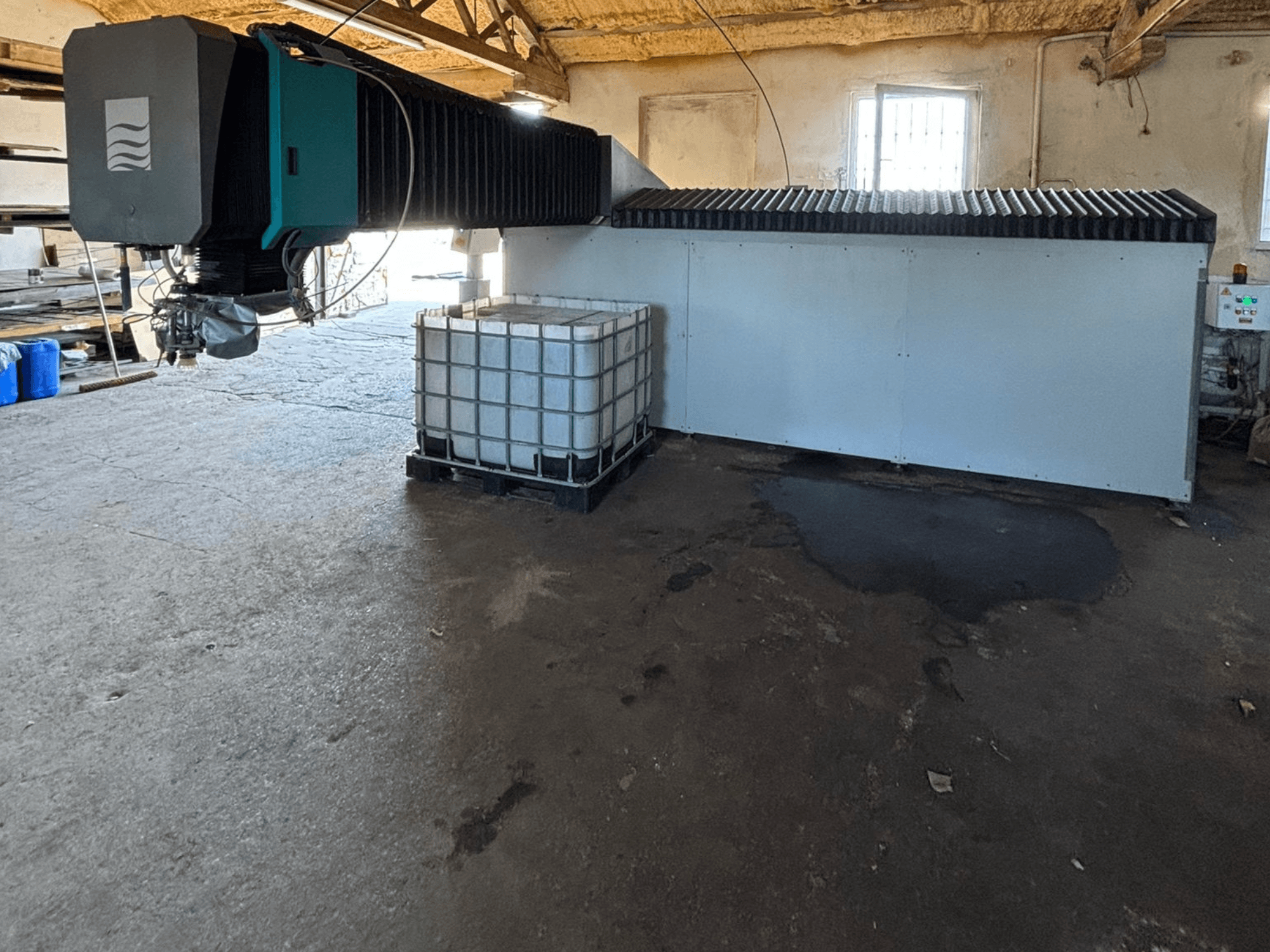 Máquina industrial de chorro de agua en un taller, vista lateral, con un gran depósito de agua y un panel de control visible al lado.