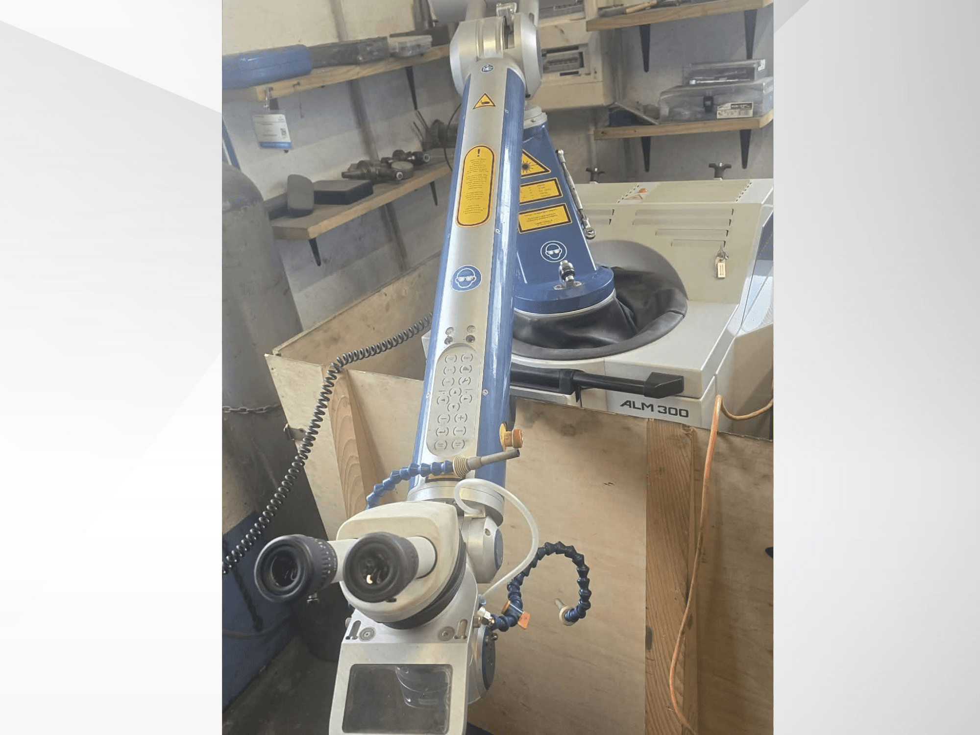 Vista frontal de la máquina de soldadura láser ALPHA LASER ALM 300, que cuenta con un brazo robótico, lentes ópticas y un panel de control.