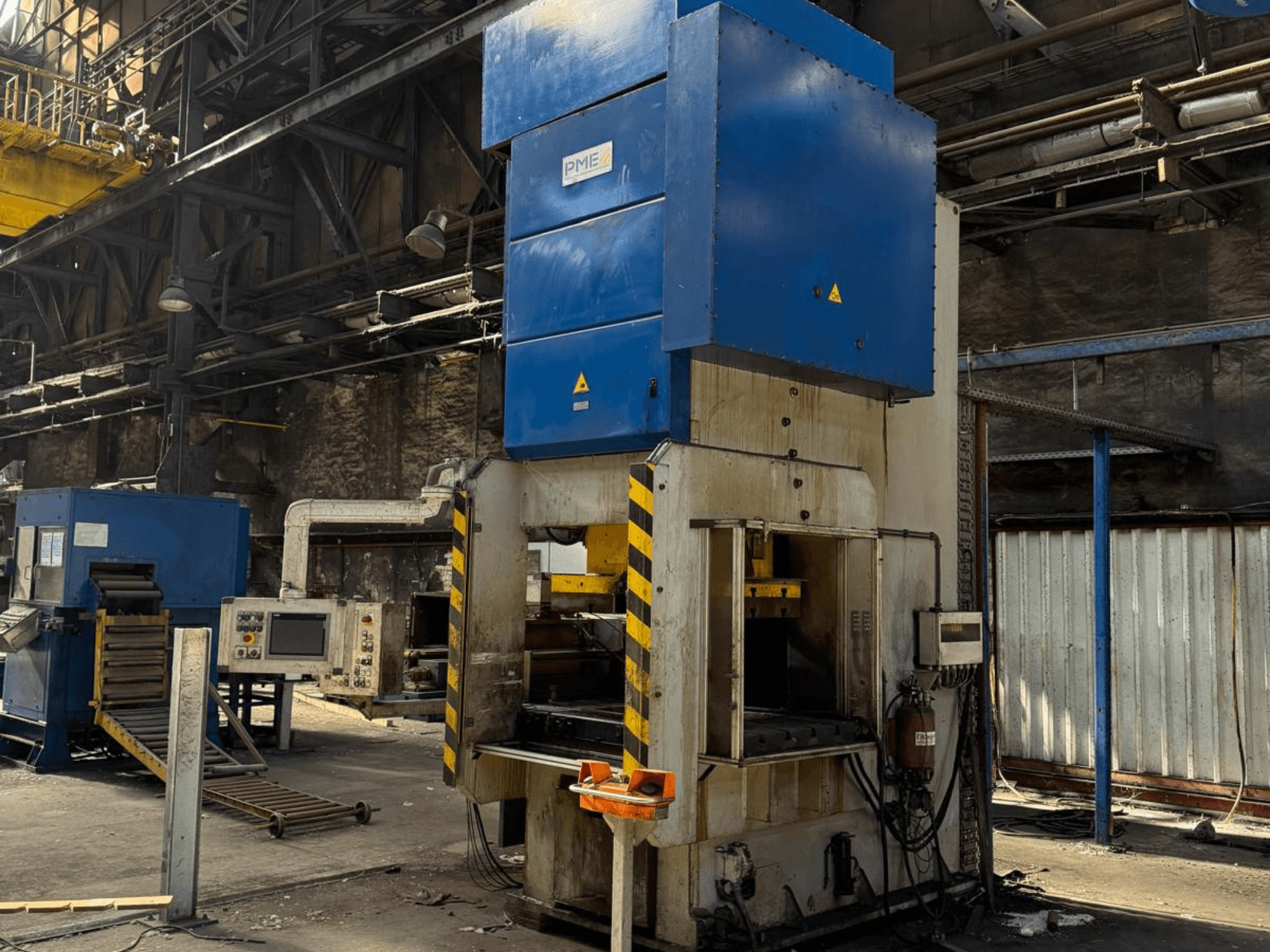 Prensa mecánica de estampación PME PE 400-1700 C, vista frontal, en la que se aprecia la parte superior azul y la base con rayas amarillas en un entorno industrial.