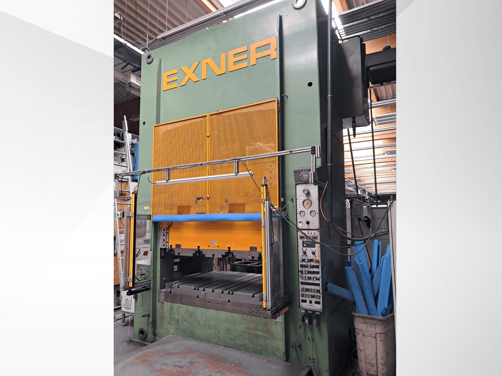 Prensa hidráulica EXNER EX SBR 150, vista frontal; con los mandos, la barra de seguridad azul y la rejilla protectora, instalada en un taller.