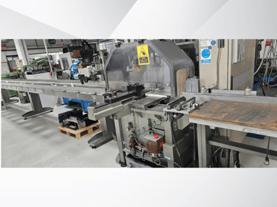 Máquina de corte industrial desde una vista lateral, con un largo transportador, panel de control y advertencias de seguridad.