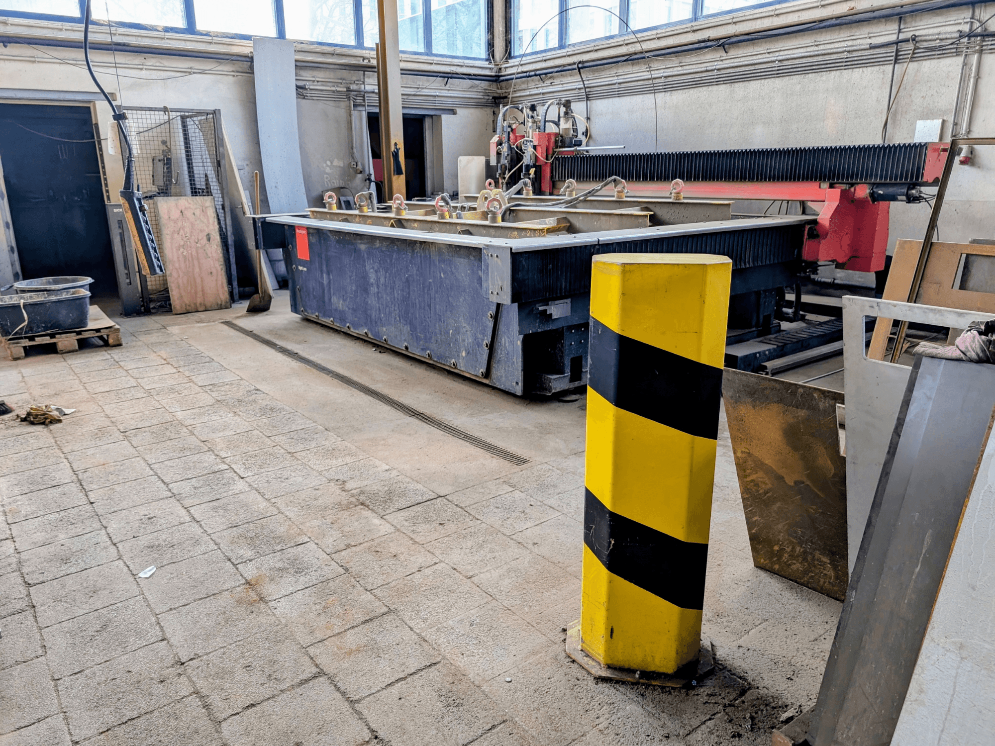 Máquina de corte por chorro de agua Bystronic Byjet L 2030 en un taller, vista lateral, con un poste de seguridad amarillo y materiales circundantes.