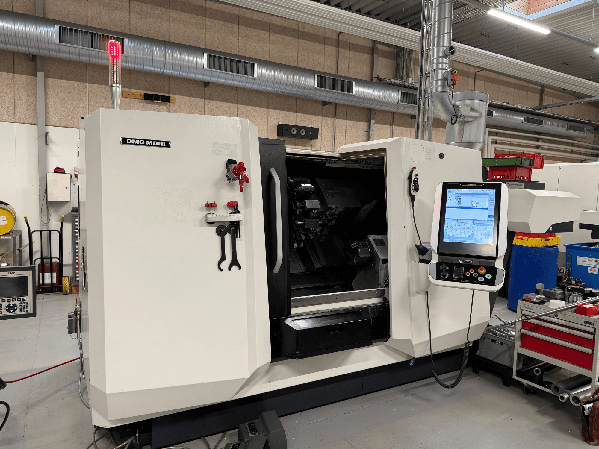 Torno horizontal DMG MORI CLX 450 V6, vista frontal en la que se aprecian el panel de control, el botón de parada de emergencia y la luz de seguridad.