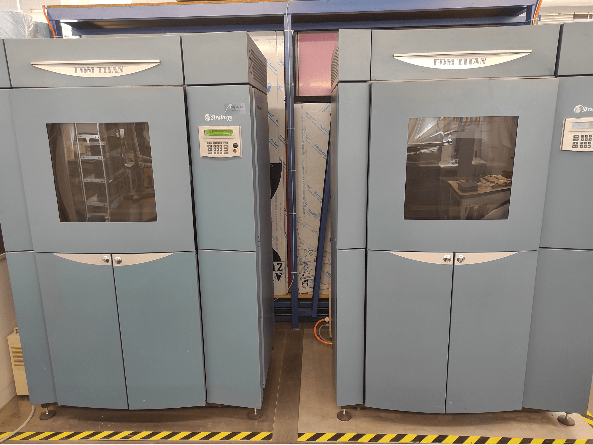 Vista frontal de la impresora 3D de plástico FDM TitanTI T0031 de Stratasys; cuenta con un panel de control y una ventana transparente.