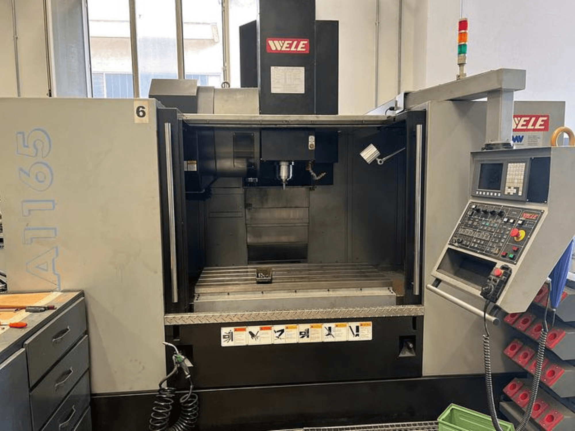 Centro de mecanizado CNC WELE A165, vista frontal, con panel de control, portaherramientas y mesa de trabajo visibles. Entorno industrial.
