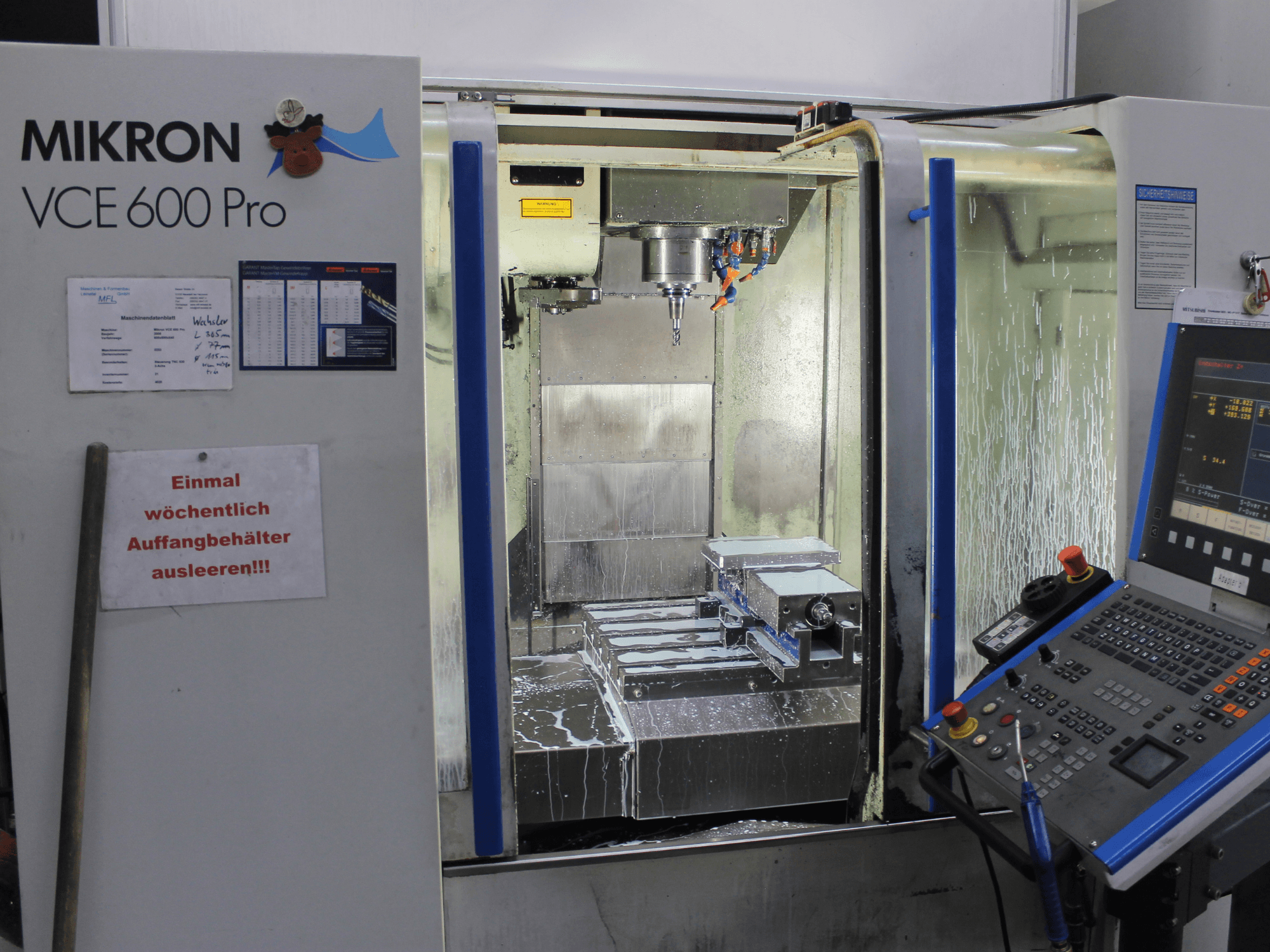 Centro de mecanizado Mikron VCE 600 Pro, vista frontal, cuenta con herramientas de corte, pulverizador de refrigerante y panel de control con botones.