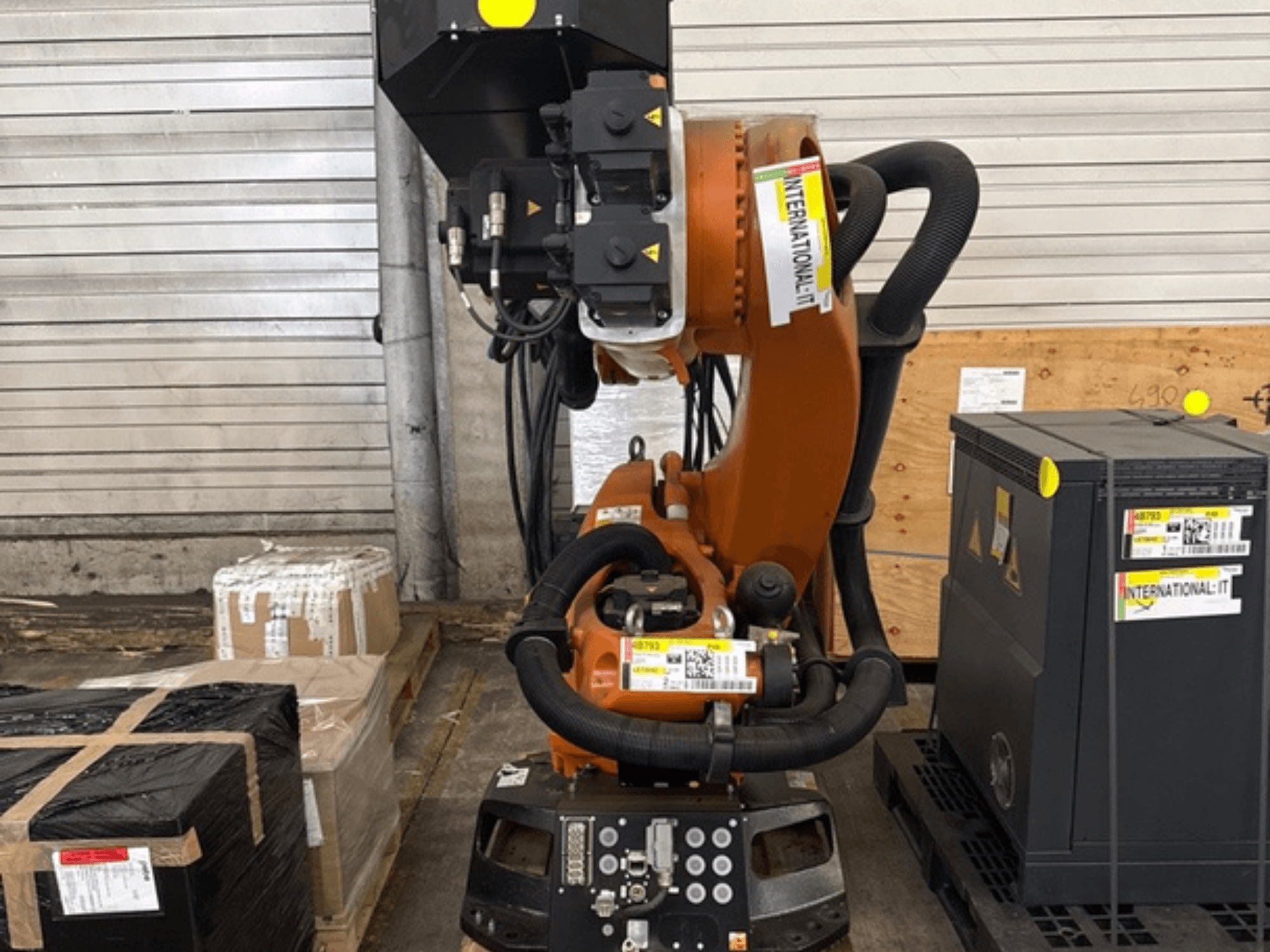 Brazo robótico adicional KUKA KR 210 R2700 en vista frontal, expuesto sobre un palé junto a paquetes y equipos.