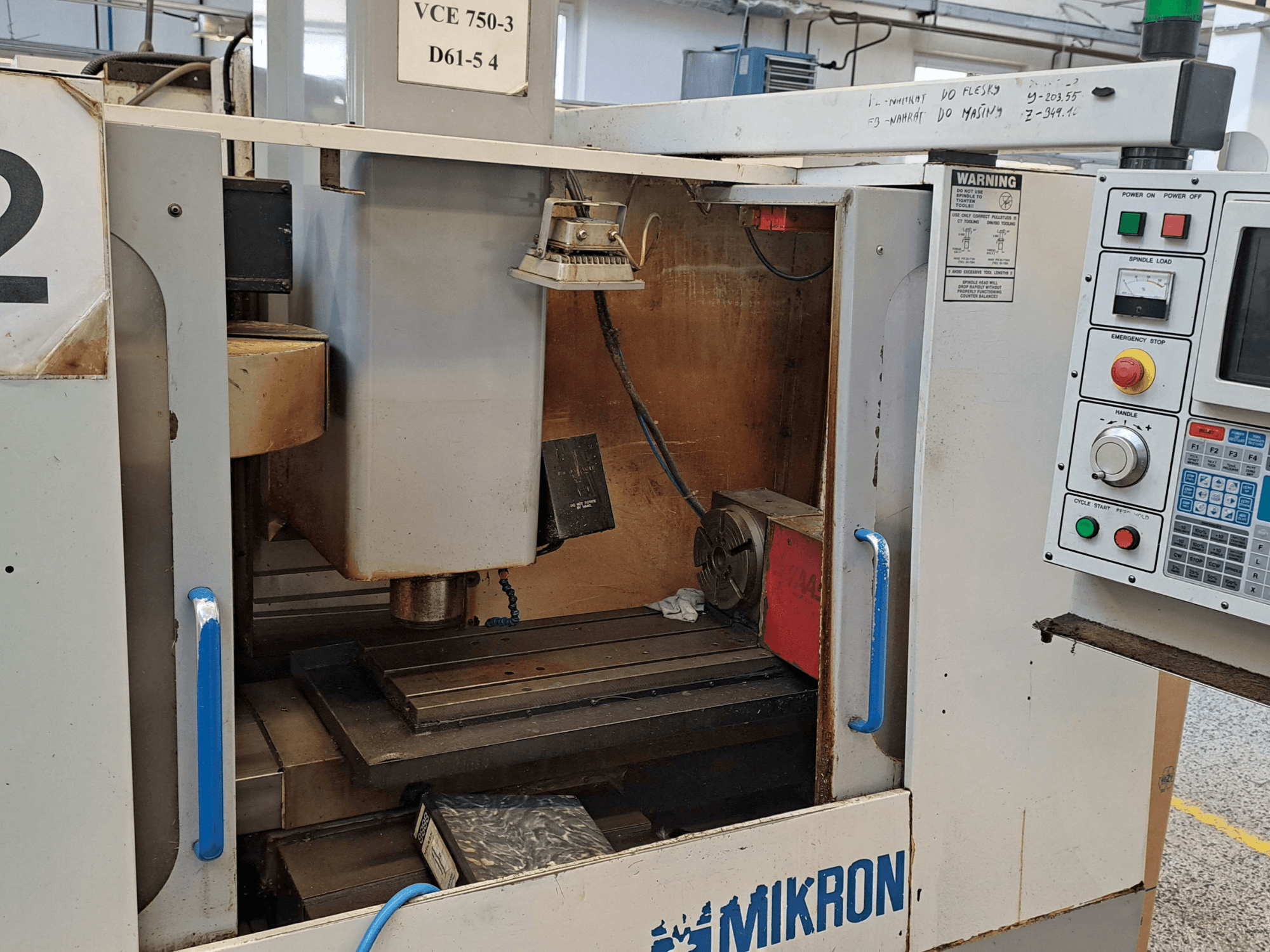 Vista frontal de una fresadora Mikron VCE 750-3, que muestra el husillo, el panel de control y la mesa de trabajo con detalles técnicos.