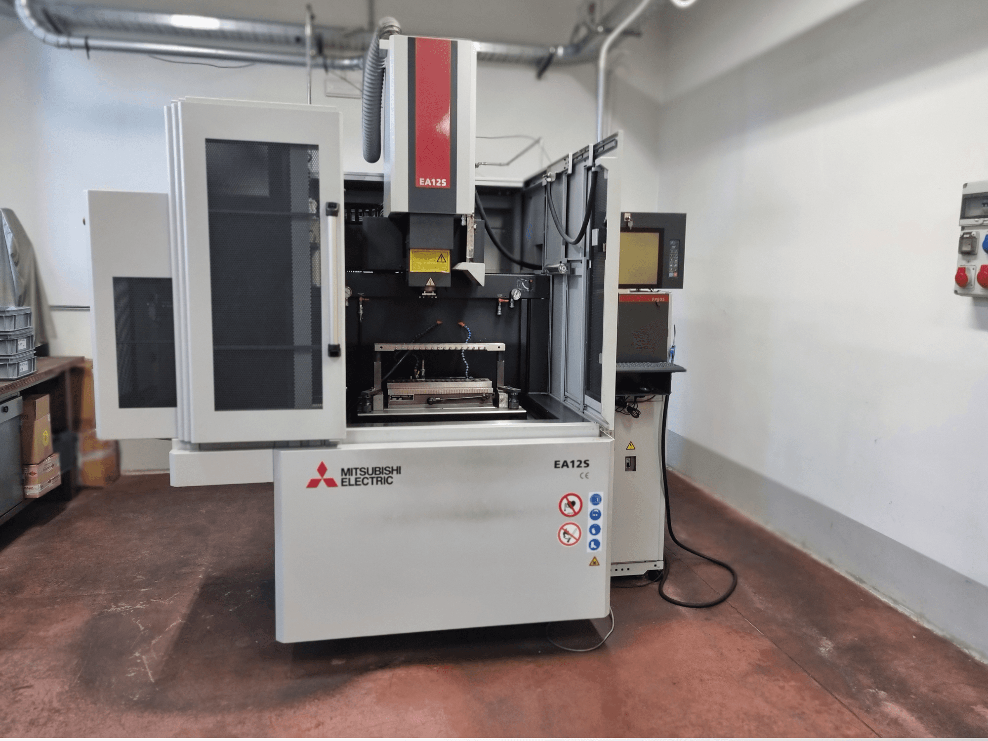 Cortadora de hilo Mitsubishi Electric EA12S, vista frontal, presenta puertas abiertas, panel de control y etiquetas de seguridad.