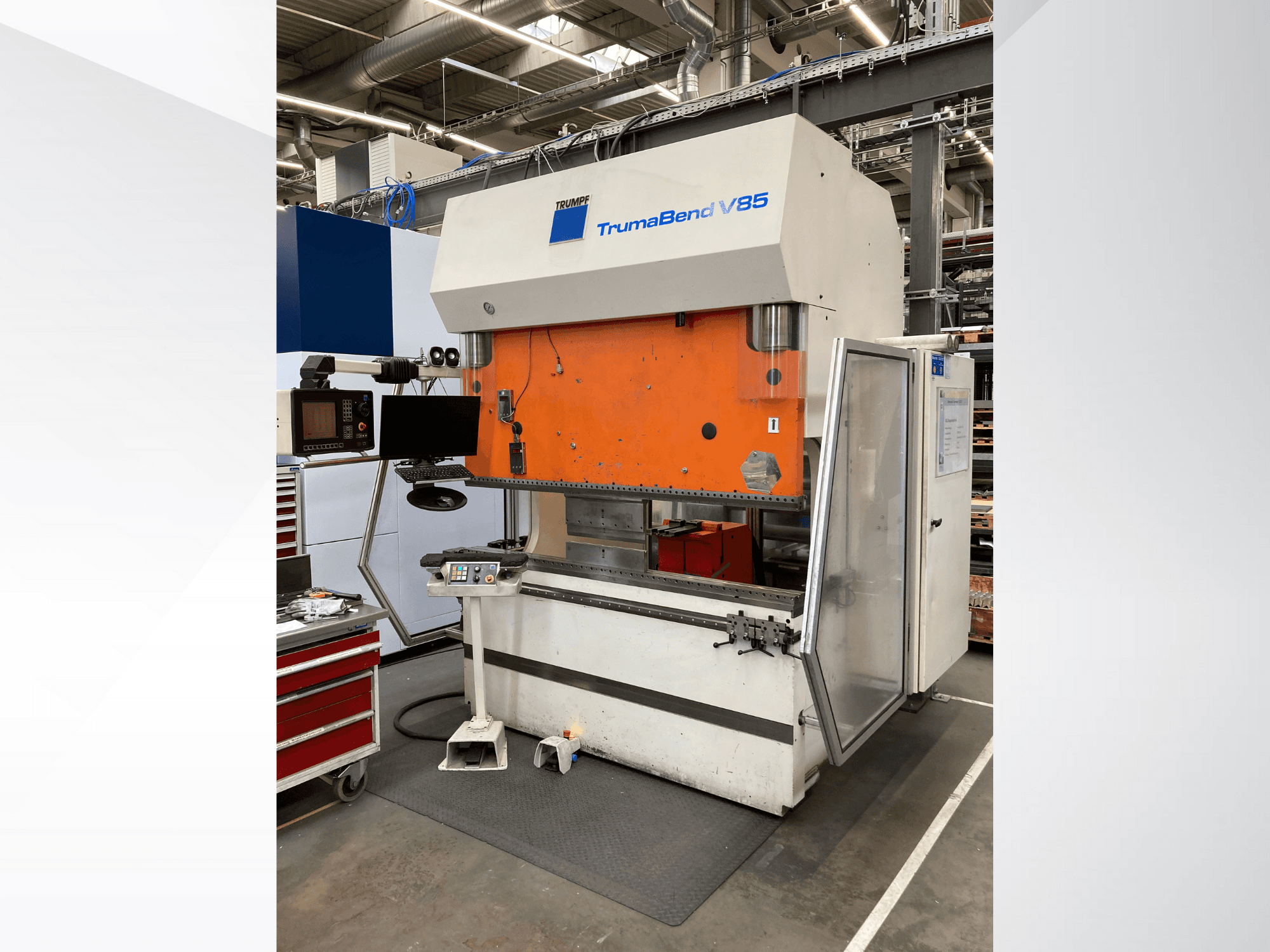 Plegadora TruMatic V85 en una fábrica, con panel frontal naranja, pantalla de control y puerta lateral abierta, vista lateral.