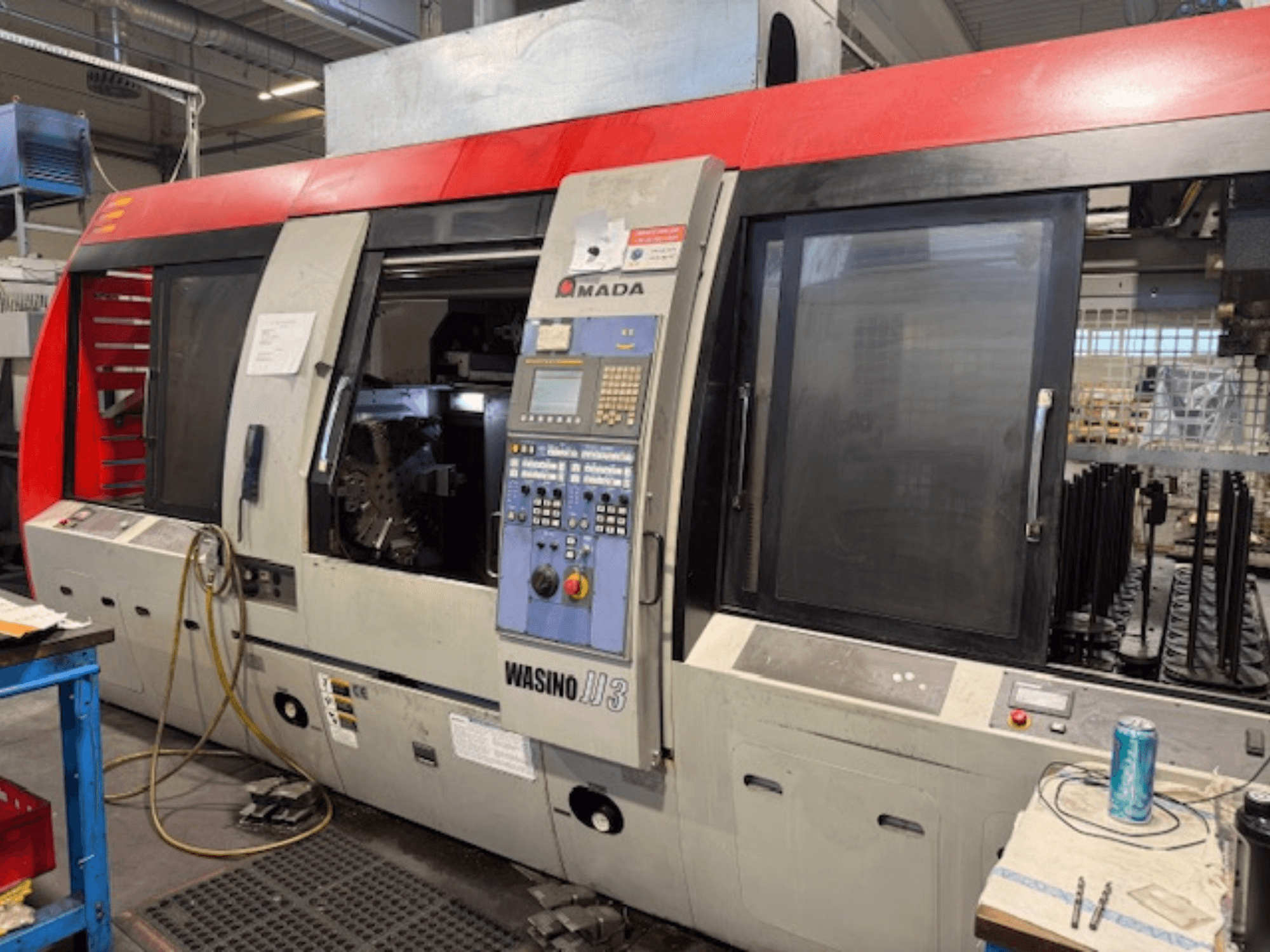 Máquina de torneado horizontal AMADA Wasino JJ3, vista frontal que muestra el panel de control y la cámara abierta para el mecanizado.