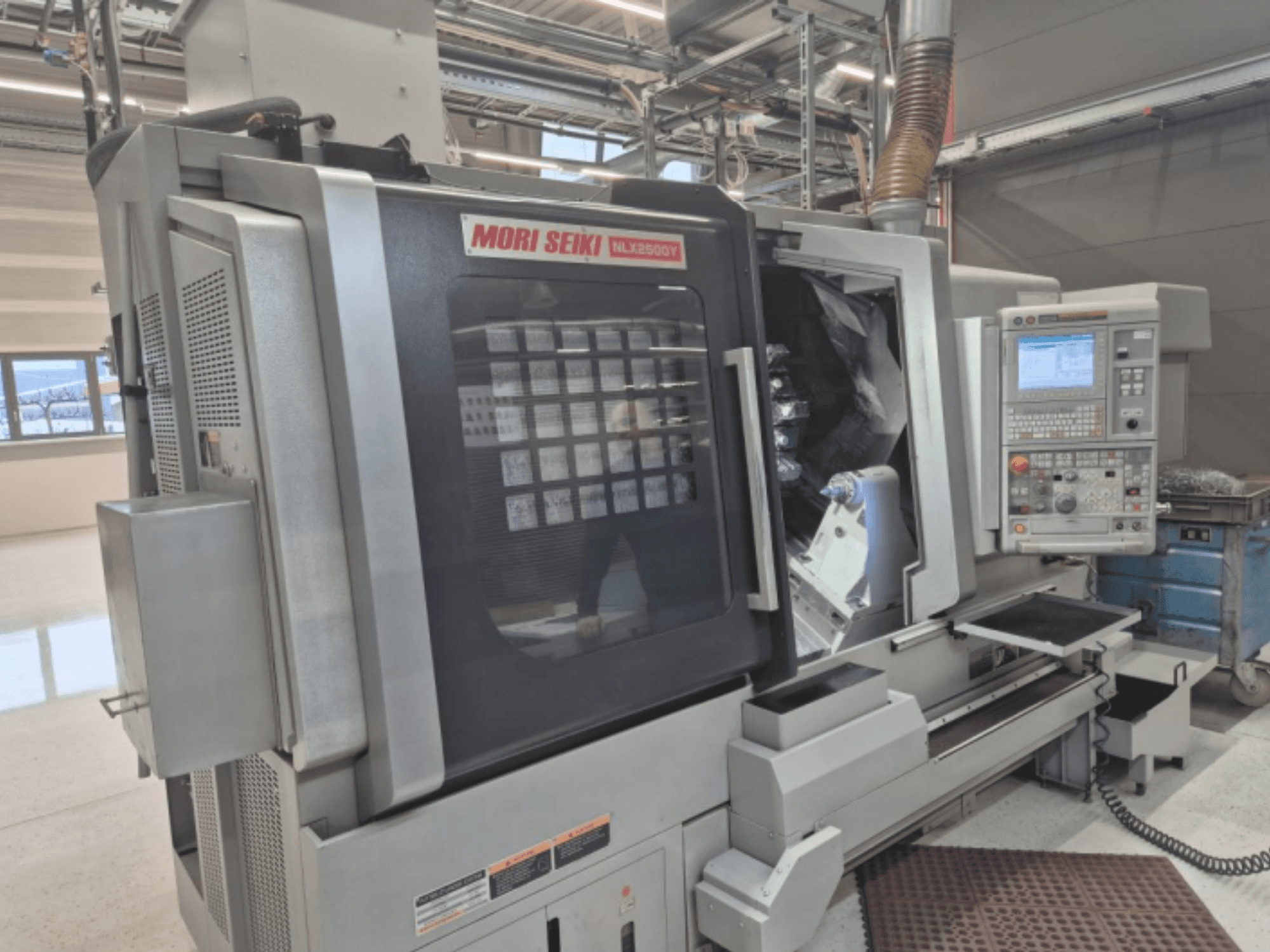 Máquina de torno CNC MORI SEIKI NL2500Y en una configuración de fábrica, vista frontal que muestra el panel de control y la cámara de la pieza de trabajo.