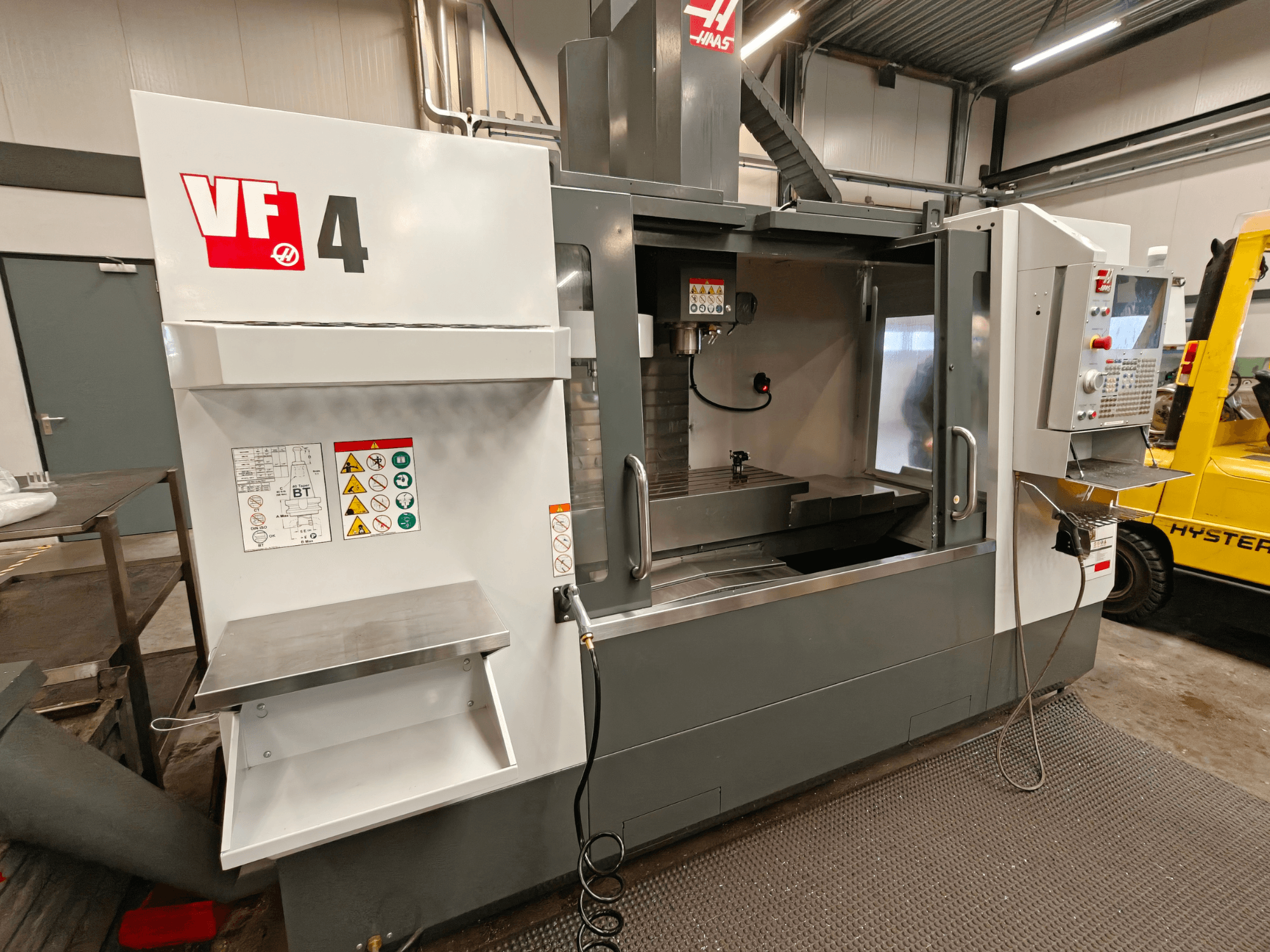 Centro de mecanizado vertical HAAS VF-4, vista frontal, con panel de control, área de trabajo y etiquetas de seguridad en el lateral.