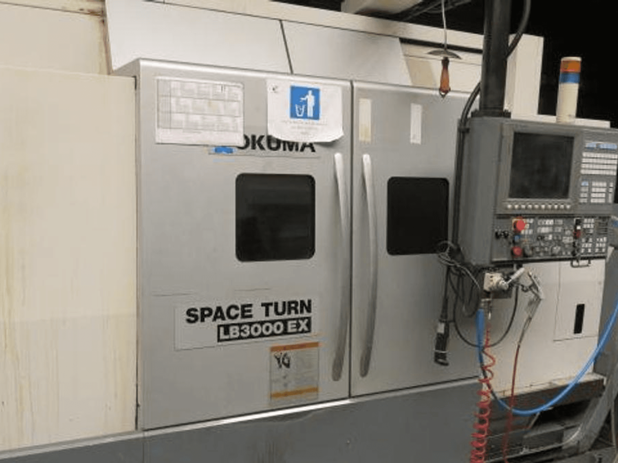 Torno CNC Okuma Space Turn LB3000 EX, vista lateral, con panel de control, dos puertas y cableado visible.